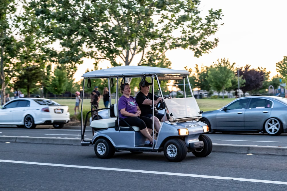 two people sitting in a golf cart on the road. 